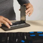 تعمیر کار در حال تعمیر گوشی باز شده با رنگ نقره ای بر روی میز چوبی کنار کیف وسایل اش